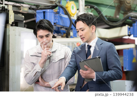 製造業の工場現場で作業着の技術者と営業が機械を見ながら見積もりや修理、メンテナンスの金額を前向き 139944238