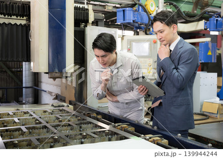製造業の工場現場で作業着の技術者と営業が機械を見ながら見積もりや修理、メンテナンスの金額を悩む考える 139944244