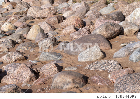 Sunlit rocky beach covered with smooth granite stones and sandy patches 139944998