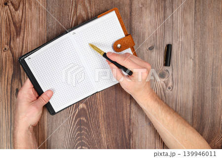 male hand writing with a pen in an open checkered notebook on a wooden table male hand writing with a pen in an open checkered notebook on a wooden table 139946011
