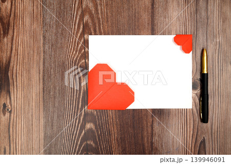 white sheet of paper with two red origami hearts and a black pen on a wooden table 139946091