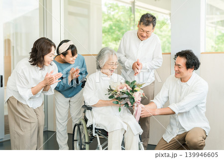 施設にいるおばあちゃんにお見舞い,お祝いで花束をプレゼントする三世代家族 139946605