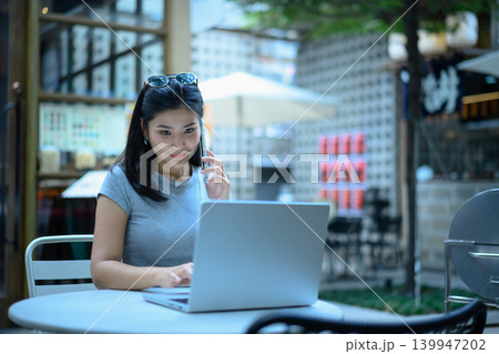 Young business woman working on a laptop and using smartphone sitting on at outdoor cafe workspace Young business woman working on a laptop and using smartphone sitting on at outdoor cafe workspace 139947202