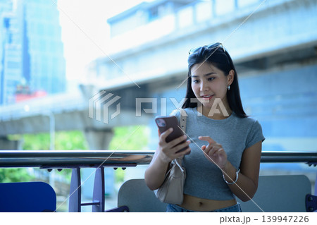 Young woman using smartphone near city transit skytrain in urban business district Young woman using smartphone near city transit skytrain in urban business district 139947226