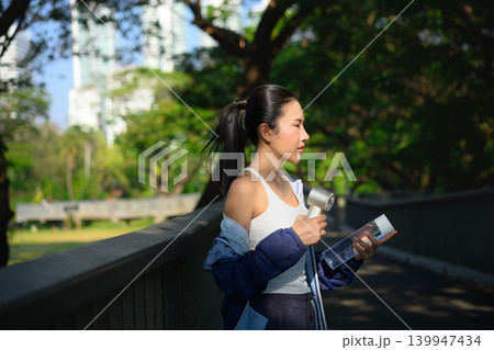 Woman holding portable fan and water bottle after workout, cooling down Woman holding portable fan and water bottle after workout, cooling down 139947434