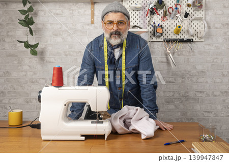 Mature male tailor standing in his clothing workshop Mature male tailor standing in his clothing workshop 139947847