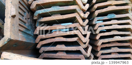A stack of traditional clay roof tiles with a rough texture and distinctive reddish brown color. 139947963