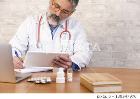 Male doctor using tablet and writing prescription Male doctor using tablet and writing prescription 139947976