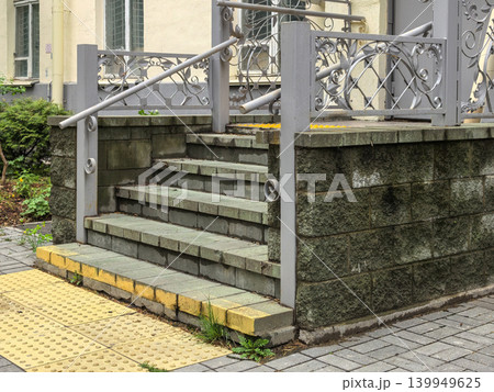 Weathered stone steps with ornate metal railing and tactile tiles 139949625