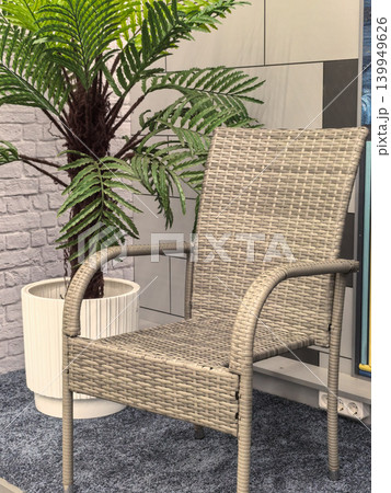 Beige wicker armchair beside artificial fern plant on gray carpet indoors Beige wicker armchair beside artificial fern plant on gray carpet indoors 139949626