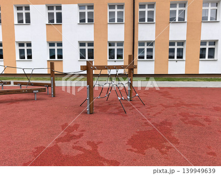 Wooden rope climbing frame on red rubber playground by school building Wooden rope climbing frame on red rubber playground by school building 139949639