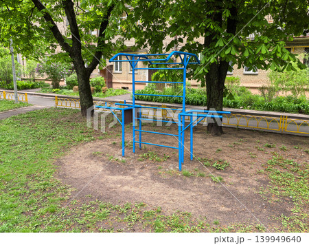 Blue street workout frame with monkey bars in green courtyard near buildings Blue street workout frame with monkey bars in green courtyard near buildings 139949640