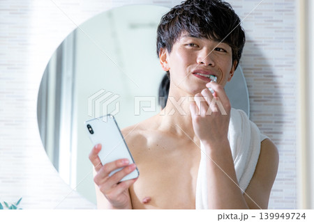 歯磨きをしながらスマホを見る若い男性 歯磨きをしながらスマホを見る若い男性 139949724