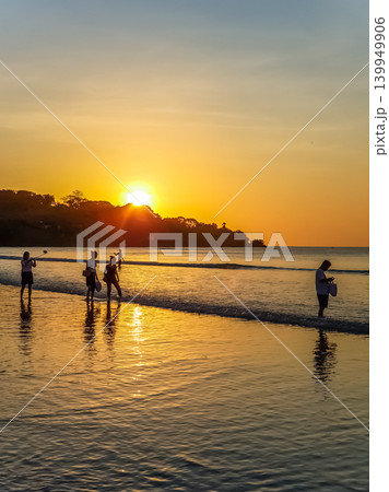 People Silhouetted on Tropical Beach at Golden Sunset with Sun Reflection on Wet Sand 139949906