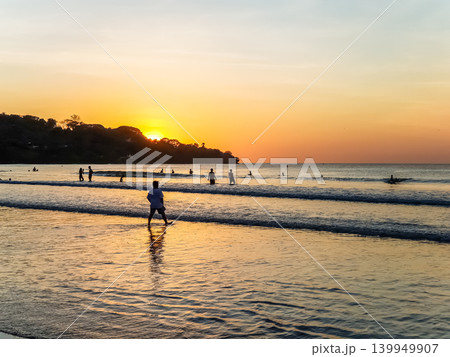 People Silhouetted on Tropical Beach at Golden Sunset with Sun Reflection on Wet Sand 139949907