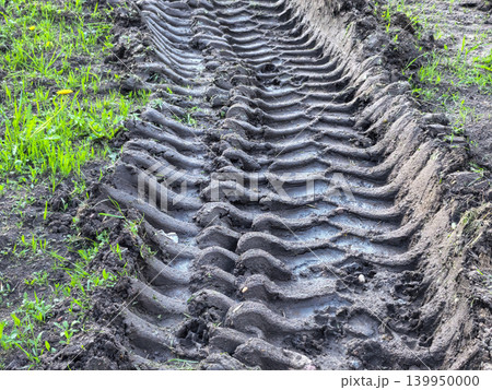 Deep tire track imprint in wet muddy ground with green grass 139950000
