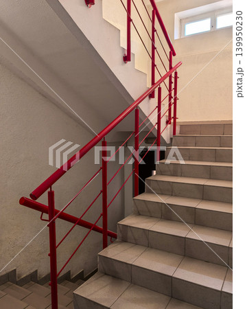 Bright red metal handrail on tiled staircase in modern building interior 139950230