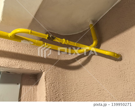 Yellow gas pipe with valve installed on ceiling corner of building hallway 139950271