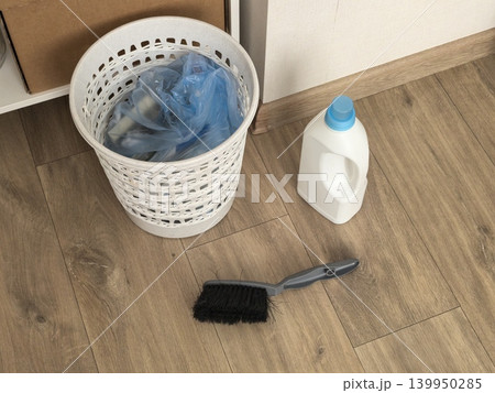 Plastic trash basket with bag detergent bottle and brush on wooden floor Plastic trash basket with bag detergent bottle and brush on wooden floor 139950285