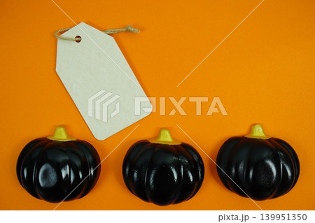 Gift tag with twine resting and three pumpkins on orange background for Halloween labels, price tags, or seasonal promotions with space for custom text. Gift tag with twine resting and three pumpkins on orange background for Halloween labels, price tags, or seasonal promotions with space for custom text. 139951350