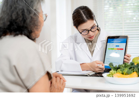 Asian woman nutritionist showing AI BMI calculator on tablet and explaining to senior patient. Asian woman nutritionist showing AI BMI calculator on tablet and explaining to senior patient. 139951692