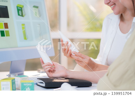 Two asian woman discussing cosmetic tube packaging sitting at modern home office. 139951704