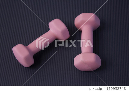 It is a pink dumbbell placed on a yoga mat. It is a pink dumbbell placed on a yoga mat. 139952748
