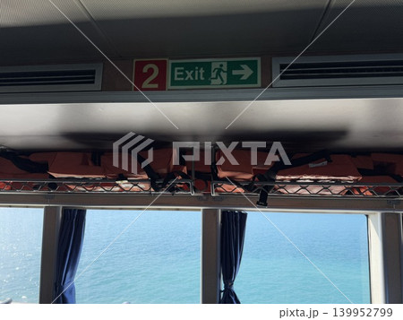 Life jackets stored on ferry ceiling with exit sign above, ocean view through windows Life jackets stored on ferry ceiling with exit sign above, ocean view through windows 139952799