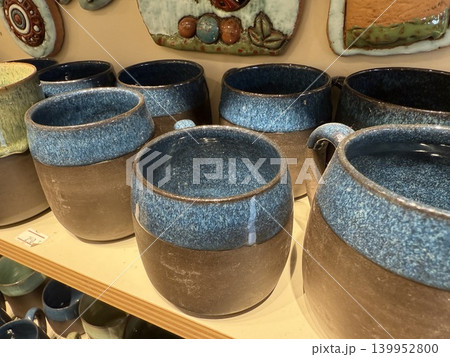 Ceramic mugs with blue glaze displayed on wooden shelf in shop, suitable as background 139952800