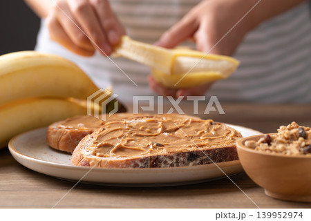 Woman's hand peeling a banana for cranberry sourdough bread, peanut butter, and granola Woman's hand peeling a banana for cranberry sourdough bread, peanut butter, and granola 139952974
