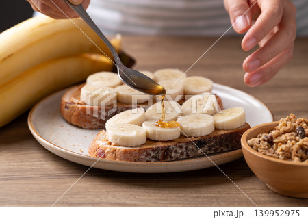 Woman's hands preparing cranberry sourdough bread with peanut butter, banana, granola and honey Woman's hands preparing cranberry sourdough bread with peanut butter, banana, granola and honey 139952975