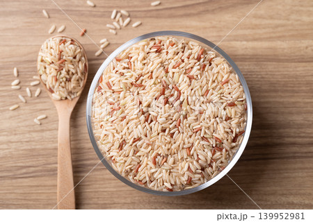 Organic Thai brown rice in a glass bowl with wooden spoon on wooden background Organic Thai brown rice in a glass bowl with wooden spoon on wooden background 139952981