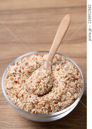 Organic Thai brown rice in a glass bowl with wooden spoon on wooden background Organic Thai brown rice in a glass bowl with wooden spoon on wooden background 139952982