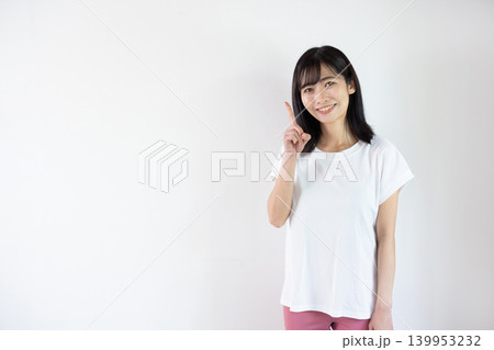 白い背景の前で人差し指を立ててカメラ目線で微笑む日本人の若い女性 139953232