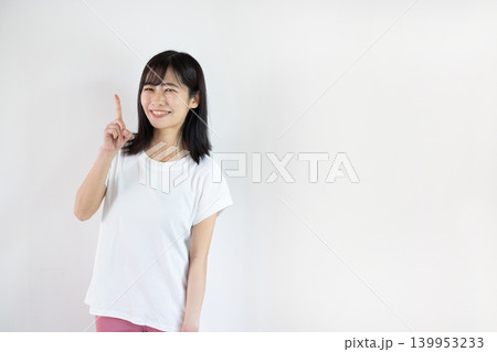白い背景の前で人差し指を立ててカメラ目線で微笑む日本人の若い女性 139953233