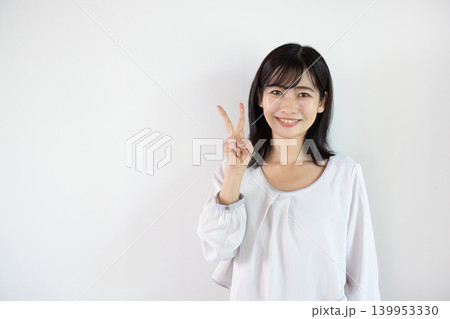 白い背景の前で指を2本立ててカメラ目線で微笑む日本人の若い女性 白い背景の前で指を2本立ててカメラ目線で微笑む日本人の若い女性 139953330