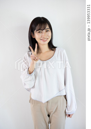 白い背景の前で指を2本立ててカメラ目線で微笑む日本人の若い女性 白い背景の前で指を2本立ててカメラ目線で微笑む日本人の若い女性 139953331