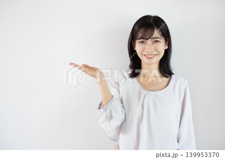 白い背景の前で手のひらを差し出し微笑む日本人の若い女性 白い背景の前で手のひらを差し出し微笑む日本人の若い女性 139953370