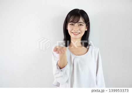 白い背景の前で手のひらを差し出し微笑む日本人の若い女性 白い背景の前で手のひらを差し出し微笑む日本人の若い女性 139953373