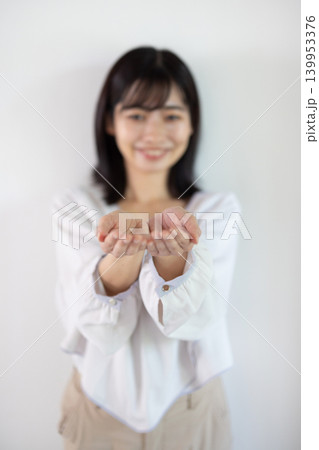 白い背景の前で手のひらを差し出し微笑む日本人の若い女性 白い背景の前で手のひらを差し出し微笑む日本人の若い女性 139953376