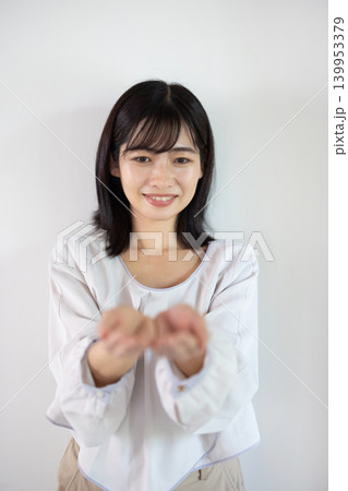 白い背景の前で手のひらを差し出し微笑む日本人の若い女性 白い背景の前で手のひらを差し出し微笑む日本人の若い女性 139953379