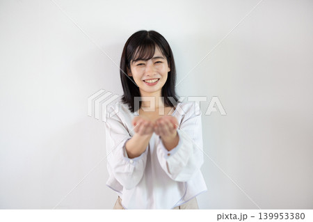 白い背景の前で手のひらを差し出し微笑む日本人の若い女性 白い背景の前で手のひらを差し出し微笑む日本人の若い女性 139953380