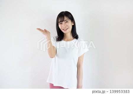 白い背景の前で手のひらを差し出し微笑む日本人の若い女性 白い背景の前で手のひらを差し出し微笑む日本人の若い女性 139953383