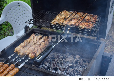 Grilled meat skewers on a barbecue grill. Smoke rises from the cooking food. Juicy pieces of meat are arranged in a metal grilling basket. 139953621
