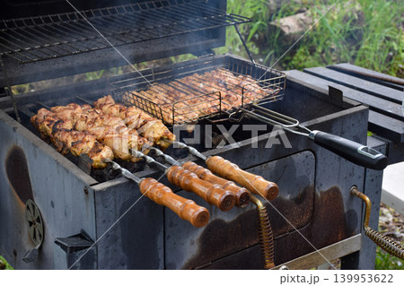 Grilled meat skewers on a barbecue grill. Smoke rises from the cooking food. Juicy pieces of meat are arranged in a metal grilling basket. 139953622
