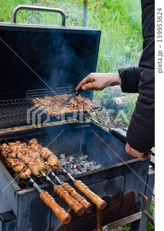Grilled meat skewers on a barbecue grill. Smoke rises from the cooking food. Juicy pieces of meat are arranged in a metal grilling basket. Grilled meat skewers on a barbecue grill. Smoke rises from the cooking food. Juicy pieces of meat are arranged in a metal grilling basket. 139953624