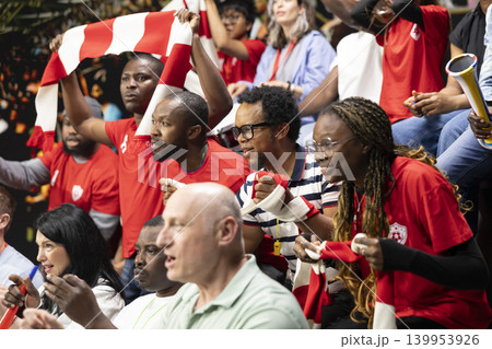Female soccer fans celebrating goal with raised arms in crowded stadium stands, red team supporters and energetic live match atmosphere in fan section. Supporters remain nervous. Female soccer fans celebrating goal with raised arms in crowded stadium stands, red team supporters and energetic live match atmosphere in fan section. Supporters remain nervous. 139953926