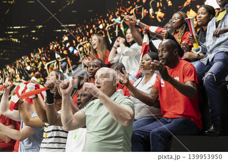 Ecstatic football supporters cheering and waving scarves after dramatic goal during live soccer match in crowded stadium stands. Joyful crowd reaction, raised fists and jumping fans. Ecstatic football supporters cheering and waving scarves after dramatic goal during live soccer match in crowded stadium stands. Joyful crowd reaction, raised fists and jumping fans. 139953950