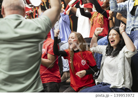Happy stadium crowd celebrating decisive winning goal during the final minutes of exciting football match. Passionate fans cheering and jumping, reacting with fan euphoria, victory moments. 139953972