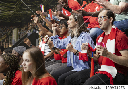 Packed stadium crowd of red team football supporters cheering with red horns and scarves during thrilling live soccer match. Emotional crowd reactions and fan chants, equality in football. Packed stadium crowd of red team football supporters cheering with red horns and scarves during thrilling live soccer match. Emotional crowd reactions and fan chants, equality in football. 139953978